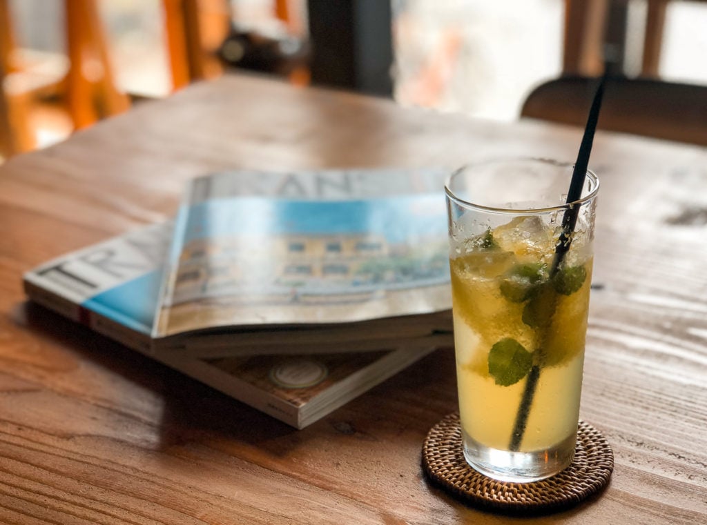 Table with a cold beverage in a glass. In the background are two magazines stacked.