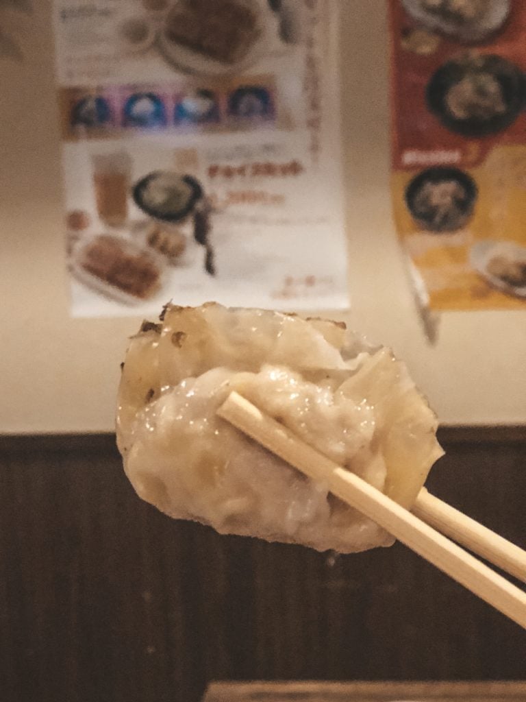 Chopsticks holding a pan-fried gyoza from Chao Chao Gyoza in Kyoto, Japan