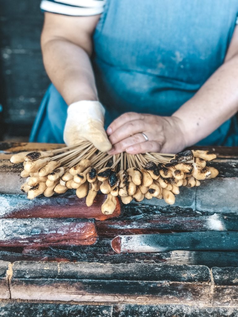 Hands holding Aburi Mochi (Japanese sweet rice cake) over a charcoal grill. From Ichiwa in Kyoto, Japan