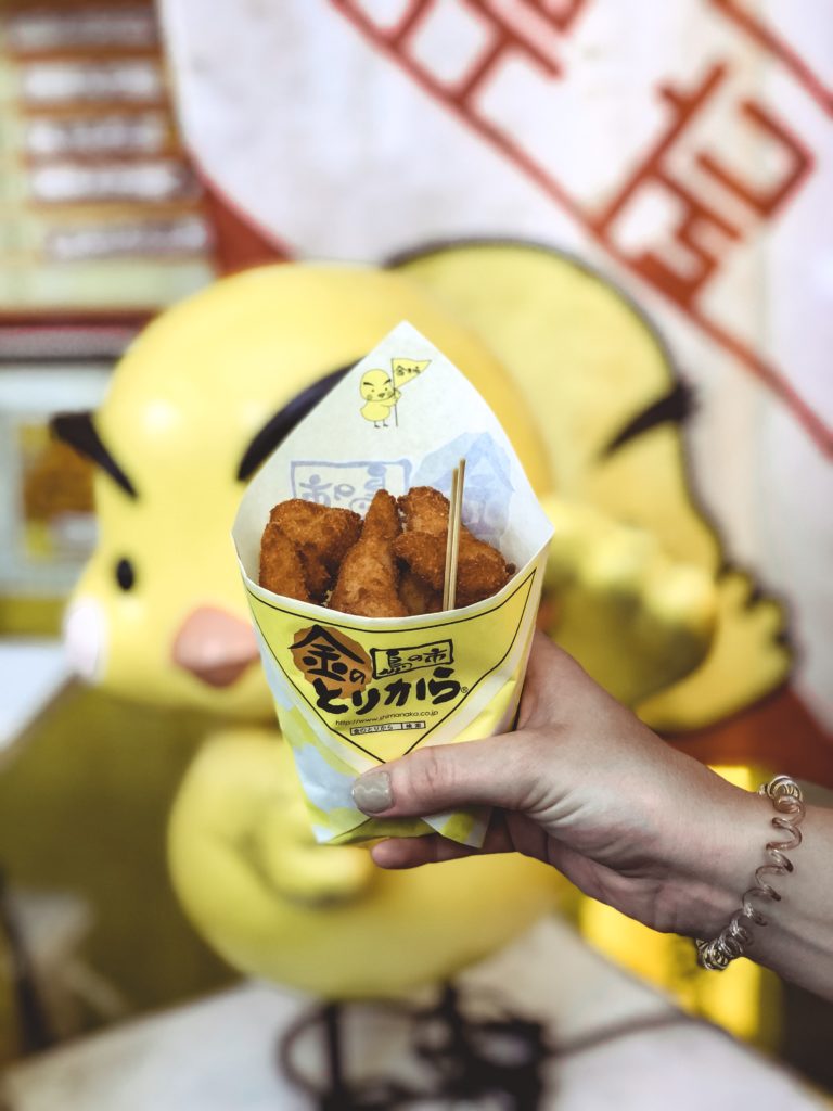 Hand holding a to-go paper holder of fried chicken.