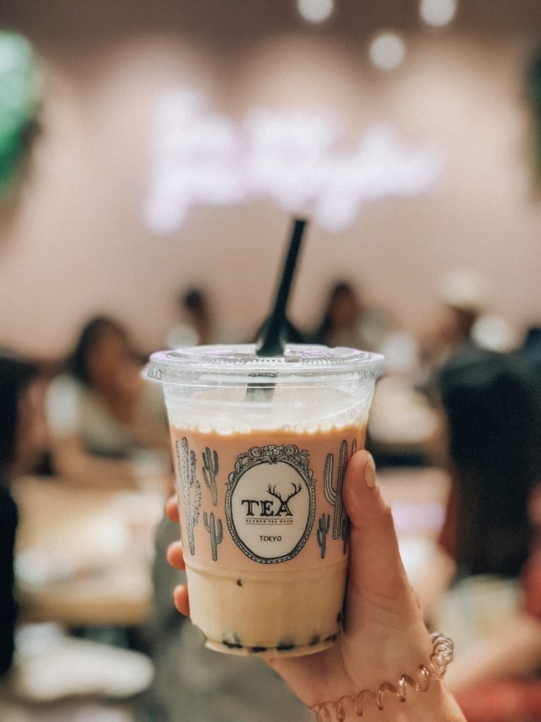Hand holding a plastic to-go cup that says "TEA, TOKYO" inside is a boba drink from Alfred Tea
