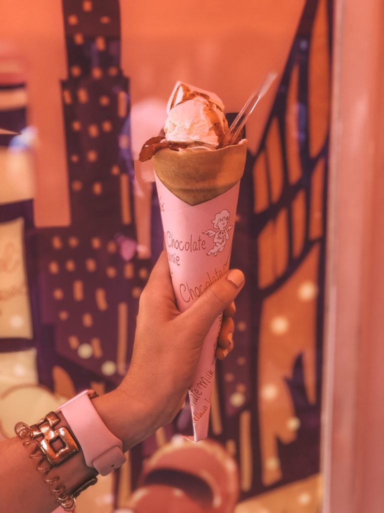 Hand holding a sweet crepe topped with ice cream and strawberry syrup.